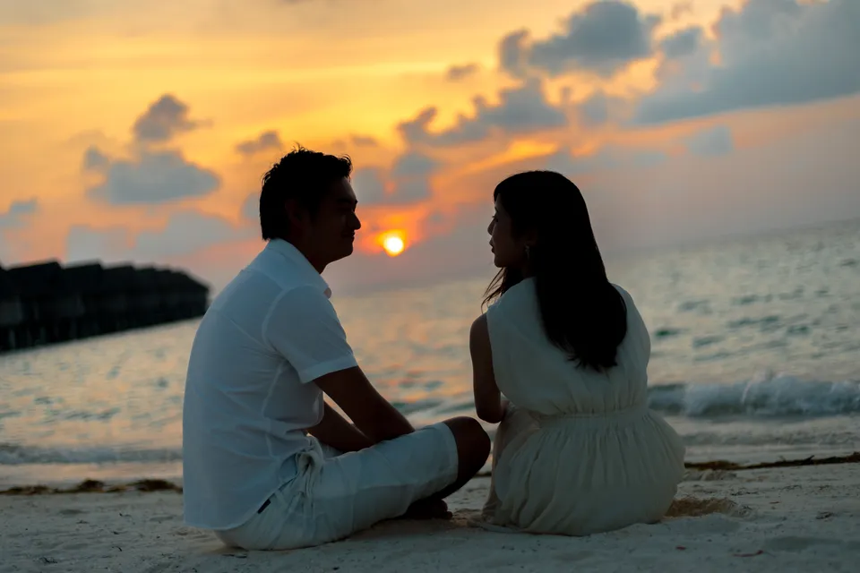 A couple sitting on the beach at sunset.