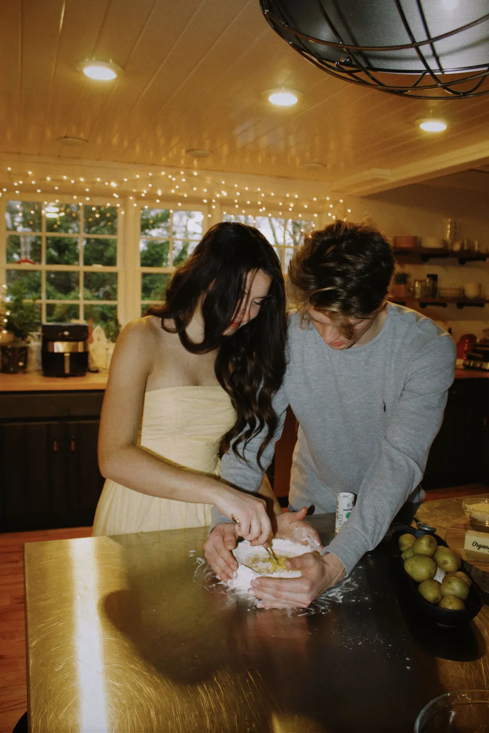 A couple making dough together in a warmly lit kitchen.