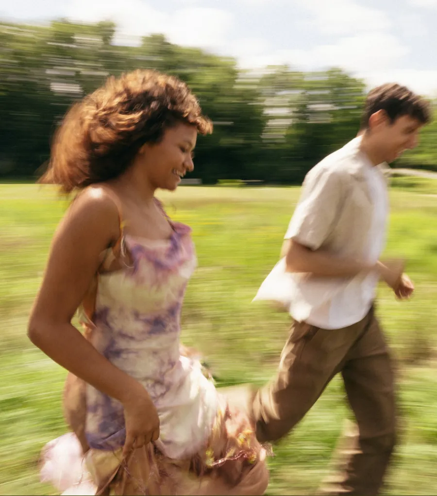 A couple running through a sunny green field.